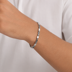 Load image into Gallery viewer, A close-up of a person's wrist wearing a silver-toned metal link bracelet against a white shirt background.